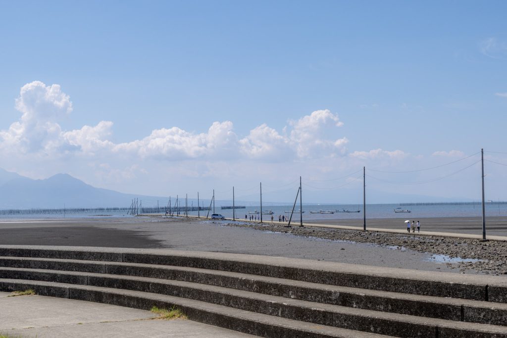 潮が引いた長部田海床路と干潟、海へ続く電柱の並ぶ道