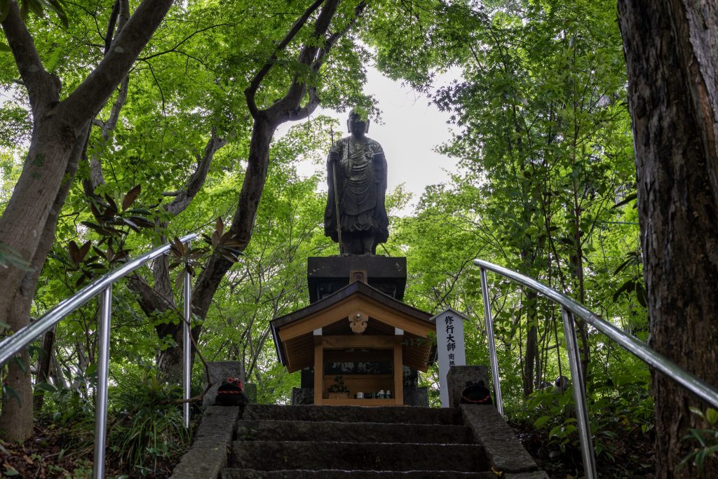 緑の木々に囲まれた如意輪寺かえる寺の階段と修行大師像