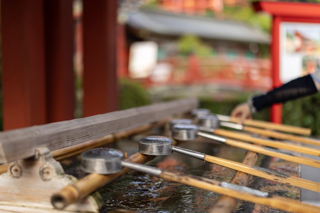 祐徳稲荷神社の手水舎で柄杓が並ぶ様子と奥に見える朱色の橋