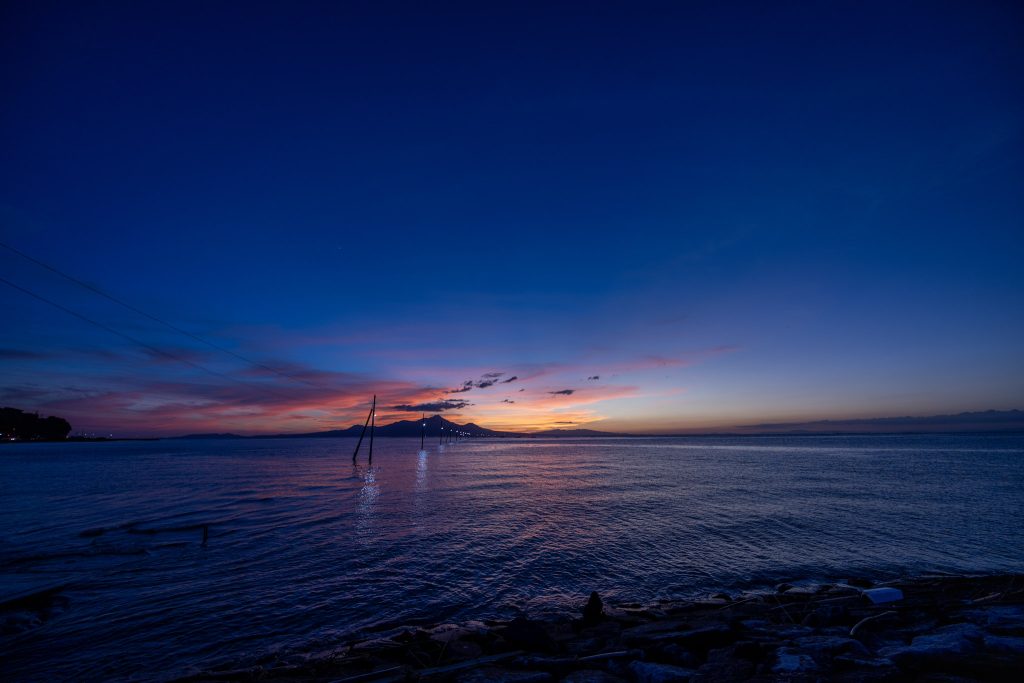 日没後の青い空と海に、明かりが灯った長部田海床路の電柱が続く夕景