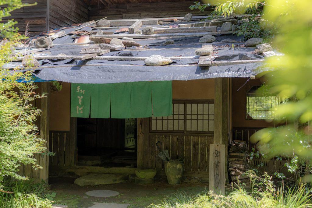 緑に囲まれた古民家そば店の、緑色ののれんが掛かる入口