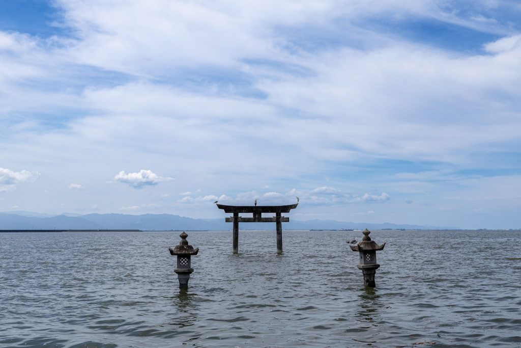 永尾剱神社の海中鳥居と2基の石灯籠を、青空と不知火海を背景に撮影した写真