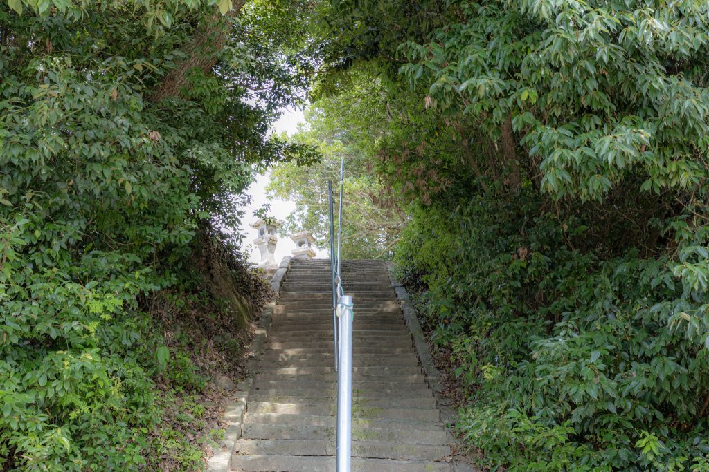 緑に囲まれた永尾剱神社の境内へ続く石段と手すりを撮影した写真
