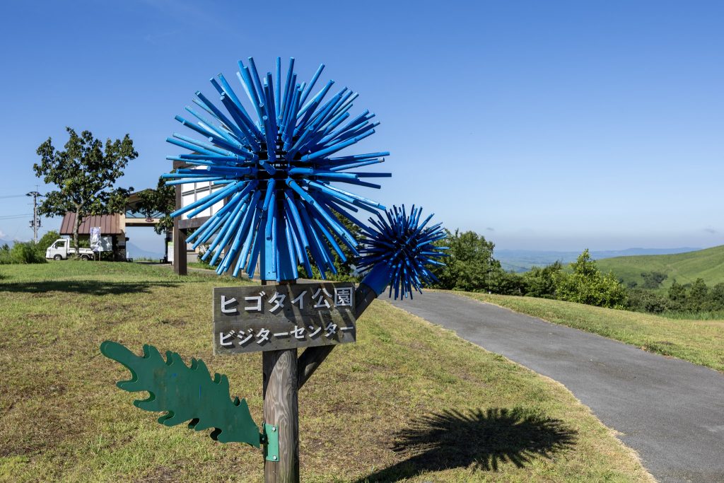 ヒゴタイ公園ビジターセンターの案内板と青いヒゴタイのオブジェ